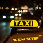 Yellow and black sign of Taxi placed on top of a car at night A yellow and black sign of Taxi placed on top of a car at night