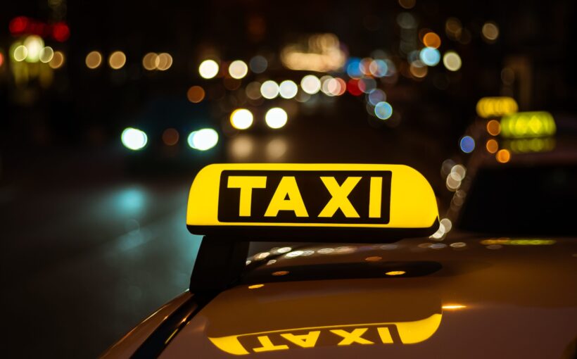 Yellow and black sign of Taxi placed on top of a car at night A yellow and black sign of Taxi placed on top of a car at night